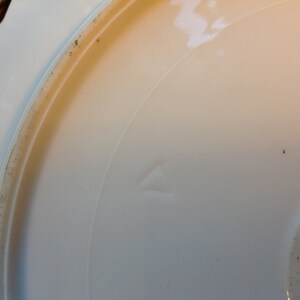 Puede incluir: Plato de cer&aacute;mica blanco con borde festoneado. El plato tiene una peque&ntilde;a marca triangular en la parte inferior.