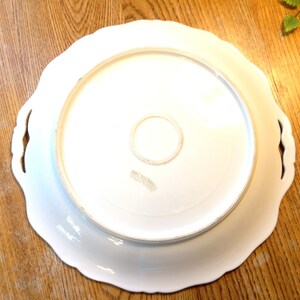 Puede incluir: Plato de servir de cer&aacute;mica blanca con bordes festoneados y dos asas. La parte inferior del plato tiene una marca circular con el texto "Made in Italy".