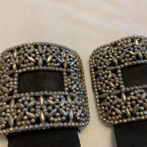 May include: Two black leather belts with silver metal buckles. The buckles are square and have a decorative design of small silver beads.