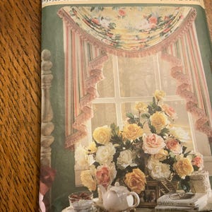 May include: A sewing pattern envelope featuring a window treatment with a floral valance and striped side drapes. The image displays a bouquet of yellow and pink roses, a white teapot, and books on a table in front of a window with curtains.