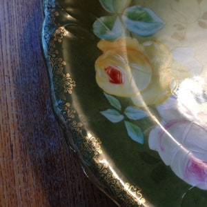 Puede incluir: Un plato de porcelana vintage con fondo verde y borde dorado. El plato est&aacute; decorado con rosas pintadas a mano en tonos de amarillo, blanco y rosa.