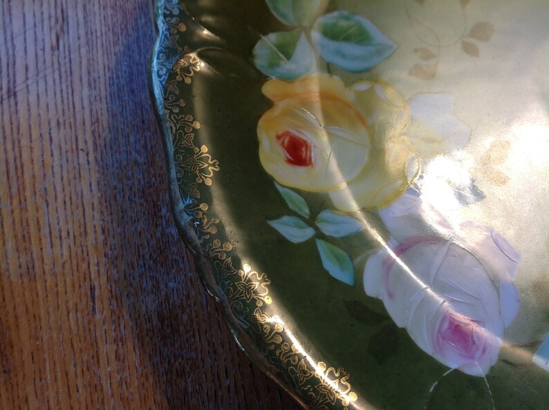 Puede incluir: Un plato de porcelana vintage con fondo verde y borde dorado. El plato est&aacute; decorado con rosas pintadas a mano en tonos de amarillo, blanco y rosa.