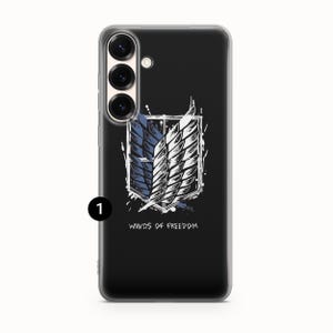 Może przedstawiać: Czarne etui na telefon z białym i niebieskim emblematem oraz napisem &bdquo;WINGS OF FREEDOM&rdquo;. Etui ma przezroczystą obw&oacute;dkę i wycięcie na aparat z trzema obiektywami.