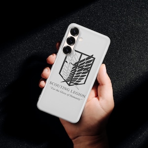 Może przedstawiać: Białe etui na telefon z emblematem Zwiadowc&oacute;w z serialu anime "Atak Tytan&oacute;w". Czarno-biały emblemat jest wyświetlany z tekstem "SCOUTING LEGION" i "For the Glory of Humanity" poniżej.