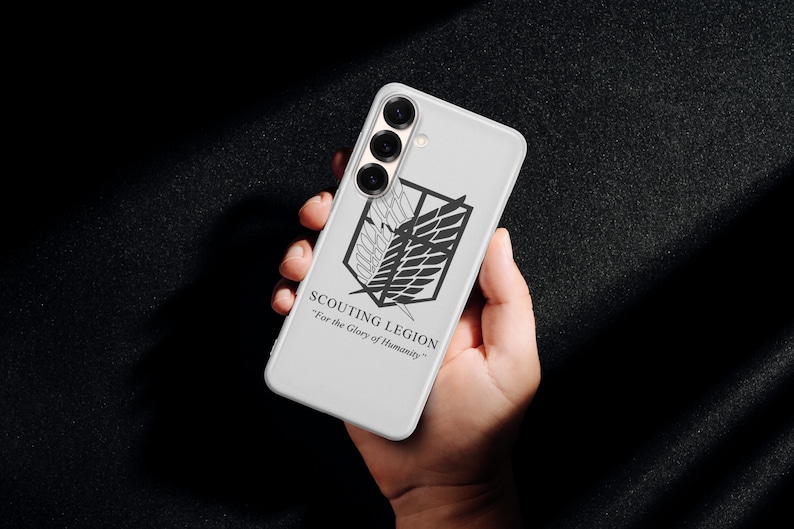 Może przedstawiać: Białe etui na telefon z emblematem Zwiadowc&oacute;w z serialu anime "Atak Tytan&oacute;w". Czarno-biały emblemat jest wyświetlany z tekstem "SCOUTING LEGION" i "For the Glory of Humanity" poniżej.