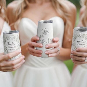 Peut inclure: Gobelets isothermes blancs avec motifs floraux et texte personnalisé. Un gobelet présente une illustration florale avec le nom "Amy". Les deux autres gobelets ont des motifs floraux et des noms. Parfait pour les enterrements de vie de jeune fille ou les cadeaux personnalisés.