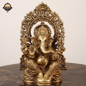 May include: A brass statue of the deity Ganesha seated in a cross-legged position. The figure features an elephant head, four arms, and ornate jewelry. Behind the figure is an intricate, arched backrest with detailed floral and scroll carvings.