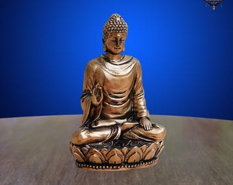 May include: A bronze-colored Buddha statue in a seated meditation pose. The statue is on a lotus flower base and has a serene expression. The background is a gradient of blue.