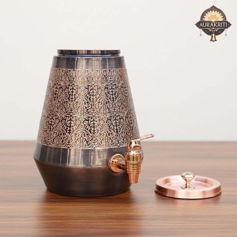 May include: A decorative copper-toned beverage dispenser with an ornate floral pattern. The dispenser has a spigot and a matching lid. The base and top are a darker shade of copper, while the middle section is a lighter copper color.
