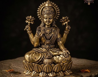 May include: A detailed brass statue of a seated deity, adorned with intricate jewelry and holding lotus flowers. The statue is positioned on a stone surface, with a dark background. The statue has a halo and is sitting on a lotus flower base.
