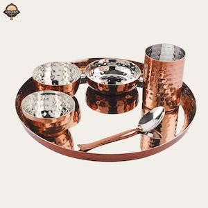 May include: A copper-toned serving set with a hammered finish. The set comprises an oval tray, three small bowls, a tall glass, and a spoon. The bowls and glass have a silver interior. The set is designed for serving food.