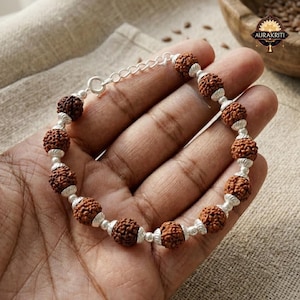May include: A brown beaded bracelet with silver accents and a chain clasp. The bracelet features multiple round, textured beads strung together with silver-toned metal. The bracelet is displayed on a hand.