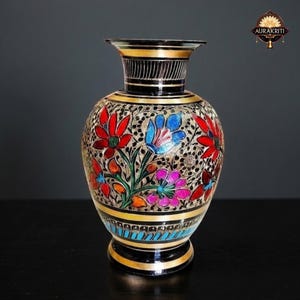 Peut inclure: Un vase décoratif avec un motif floral. Le vase a un col et une base noirs avec des accents dorés. Le corps du vase est orné de fleurs rouges, bleues et roses. Le vase mesure environ 20 cm de haut.