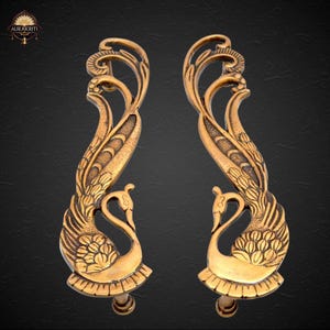 May include: Two ornate, gold-colored door handles with a peacock design. Each handle features a peacock at the base and a flowing, stylized feather design. The handles are symmetrical and detailed, with a vintage aesthetic.