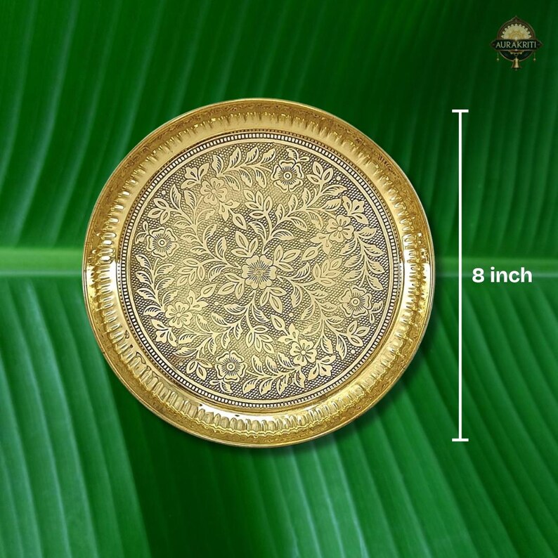 May include: A gold-colored, round decorative plate with an intricate floral pattern. The plate is 8 inches in diameter and has a detailed border. The background is a vibrant green, creating a striking contrast. The plate is likely made of metal.