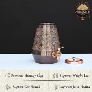 May include: A copper-colored water dispenser with an ornate floral pattern on the upper portion. It features a spigot and a lid. The dispenser is on a white surface with a dark background. The image also includes text that says "Promotes Healthy Skin" and "Supports Weight Loss."