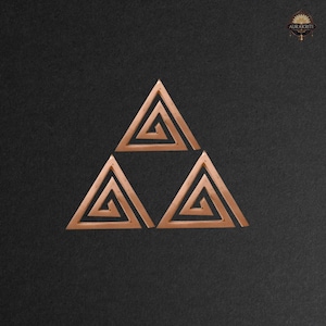 May include: Three copper-coloured, open-frame triangles arranged in a triangular formation. Each triangle features an interior spiral design. The background is a dark, textured surface. The logo "AURAKRITI" is in the upper right corner.