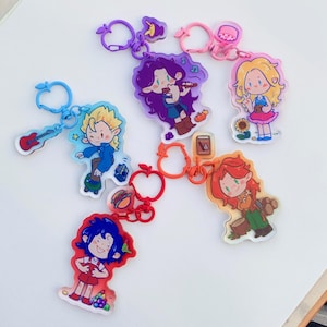 May include: A collection of colorful acrylic keychains featuring cartoon characters. Each keychain has a different character design, with various colors and shapes. The keychains are attached to metal rings.