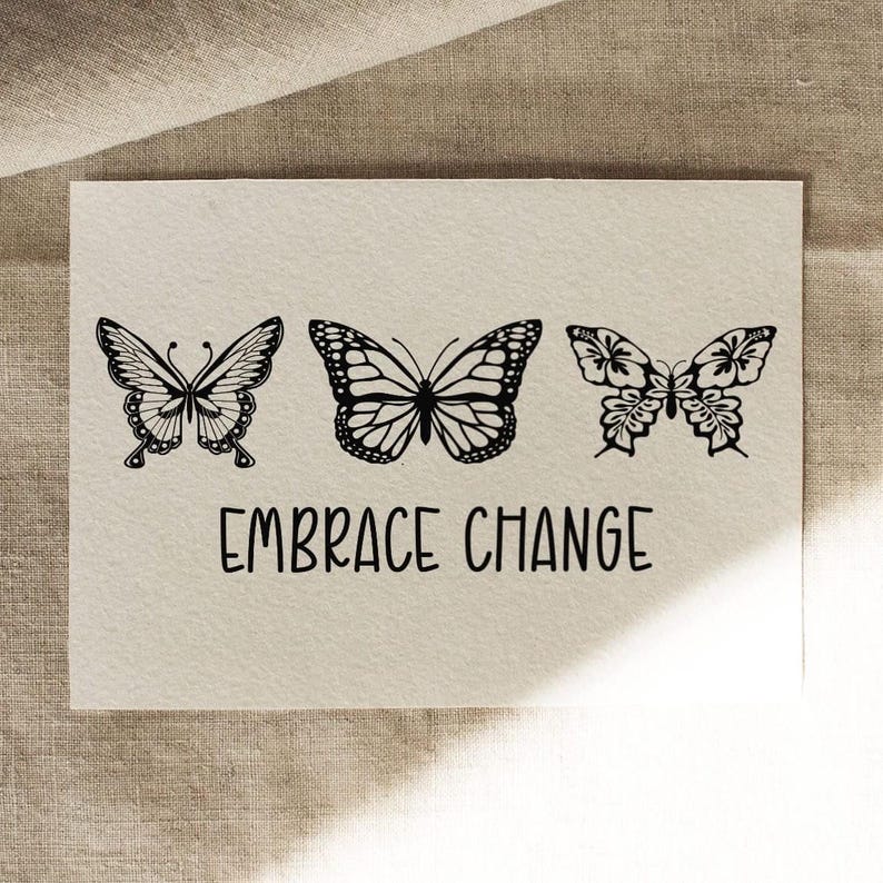 Puede incluir: Una tarjeta color crema presenta tres ilustraciones de mariposas negras sobre la frase "EMBRACE CHANGE" en una fuente manuscrita. Las mariposas tienen diferentes dise&ntilde;os, cada una con patrones de alas detallados.