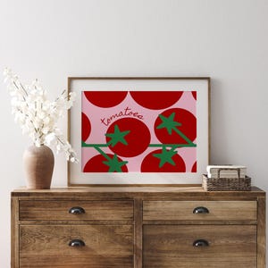 May include: A framed print featuring a repeating pattern of red tomatoes with green stems and leaves on a pink background. The word "tomatoes" is written in cursive. The artwork is displayed on a wooden dresser.