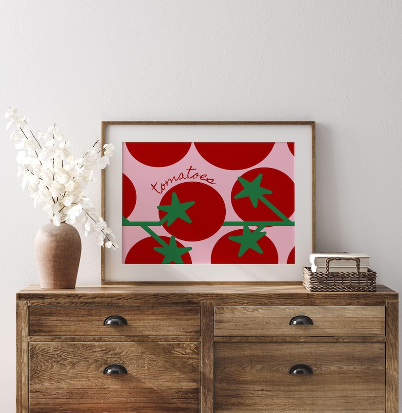 May include: A framed print featuring a repeating pattern of red tomatoes with green stems and leaves on a pink background. The word "tomatoes" is written in cursive. The artwork is displayed on a wooden dresser.