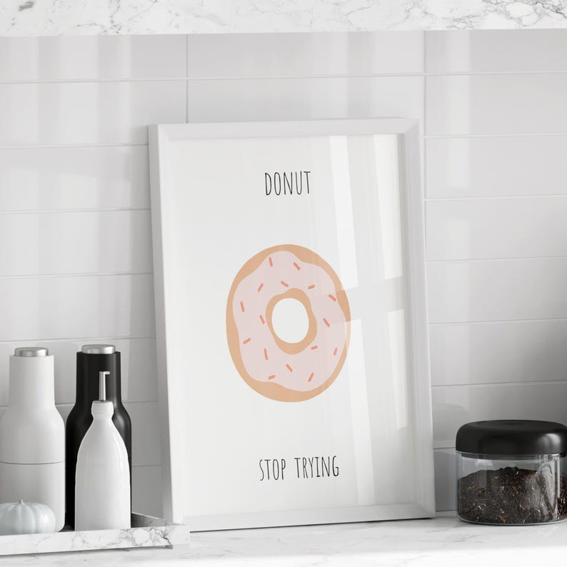 Puede incluir: Una impresi&oacute;n enmarcada con un borde blanco presenta un donut de dibujos animados con glaseado rosa y chispas. Las palabras "DONUT" y "STOP TRYING" est&aacute;n impresas encima y debajo del donut. Sobre una superficie de baldosas blancas.