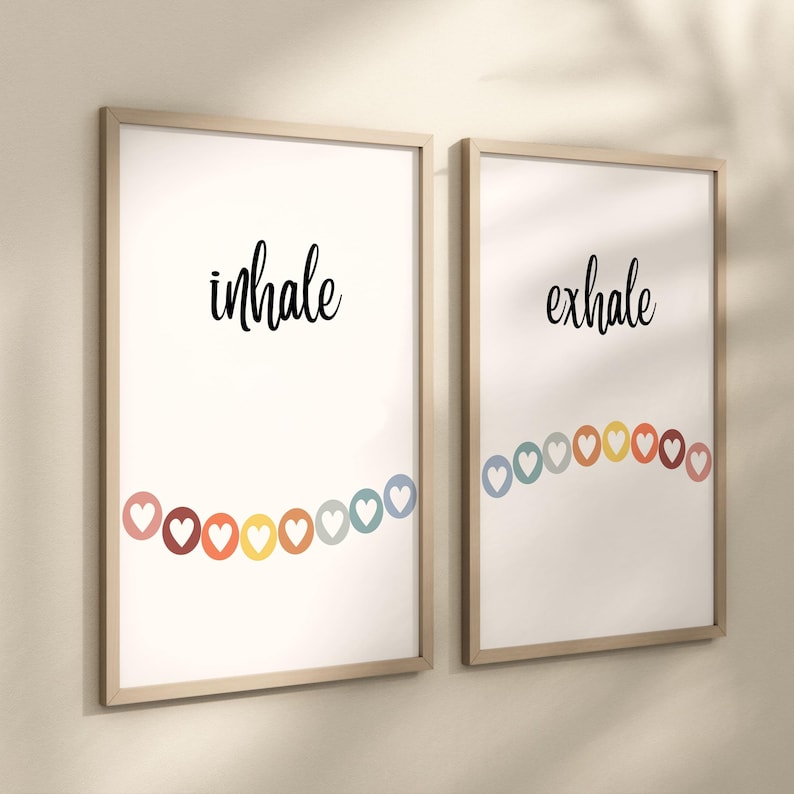 Puede incluir: Dos impresiones art&iacute;sticas enmarcadas con las palabras "inhale" y "exhale" en escritura negra. Cada impresi&oacute;n presenta una cadena de corazones coloridos. Los marcos son de madera clara.