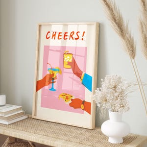 May include: A framed art print with the word "CHEERS!" in red. The illustration depicts three hands holding a cocktail, a glass of ice, and a slice of pizza. The background is pink with a window design.