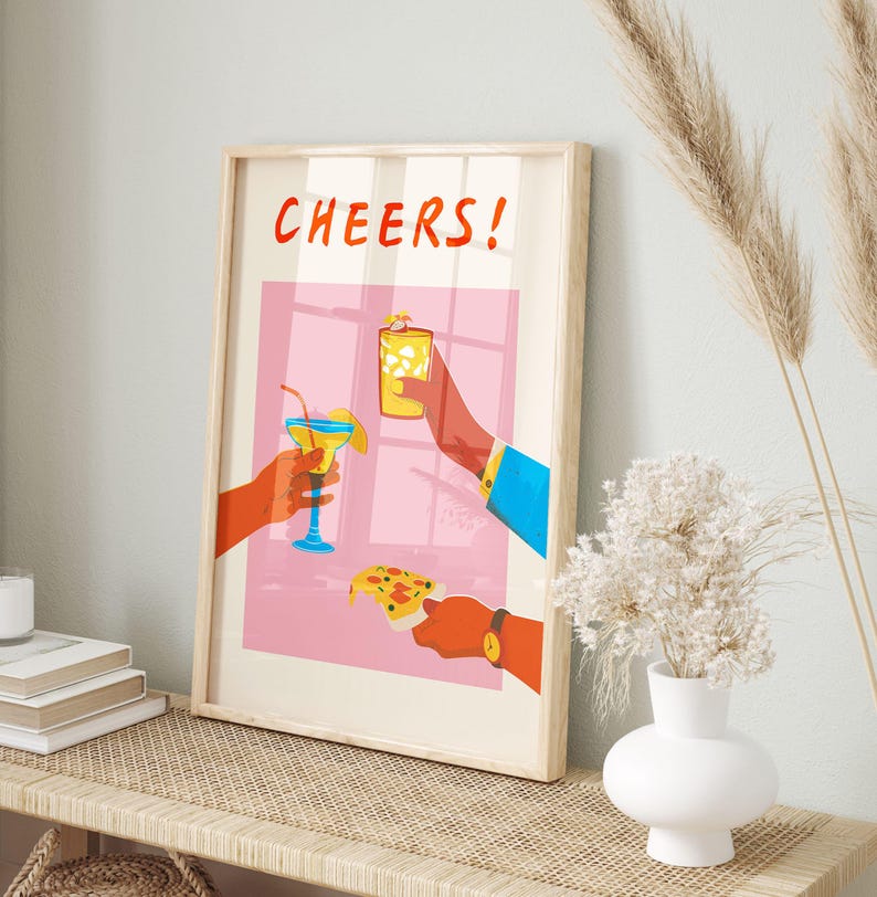 May include: A framed art print with the word "CHEERS!" in red. The illustration depicts three hands holding a cocktail, a glass of ice, and a slice of pizza. The background is pink with a window design.