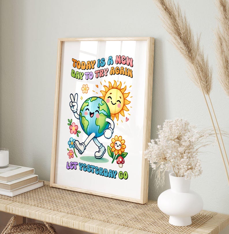Puede incluir: Una impresi&oacute;n enmarcada con una ilustraci&oacute;n alegre. La obra presenta un personaje de la Tierra sonriente haciendo el signo de la paz, un sol sonriente y el texto "TODAY IS A NEW DAY TO TRY AGAIN LET YESTERDAY GO" en letras coloridas. El marco es marr&oacute;n claro.