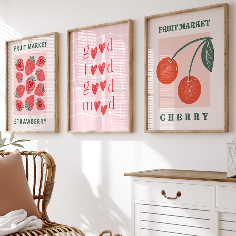 May include: Three framed art prints with a fruit market theme. One print features strawberries, another has the words "good mood", and the third displays cherries. The prints have a light pink background and are in wooden frames.