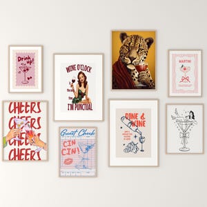 May include: A collection of framed art prints with a vintage cocktail theme. The prints feature illustrations of cocktails, a jaguar holding a drink, and text like "Drink Up!" and "Wine O'Clock". The color palette includes pink, red, and beige.