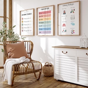 Puede incluir: Tres impresiones enmarcadas con texto: "5-4-3-2-1 Grounding Technique", "7 Reglas de la Vida" y "Estrategias Calmantes". Cuelgan sobre un mueble blanco y una silla de mimbre con un coj&iacute;n y una manta. Una cesta tejida est&aacute; en el suelo de madera.