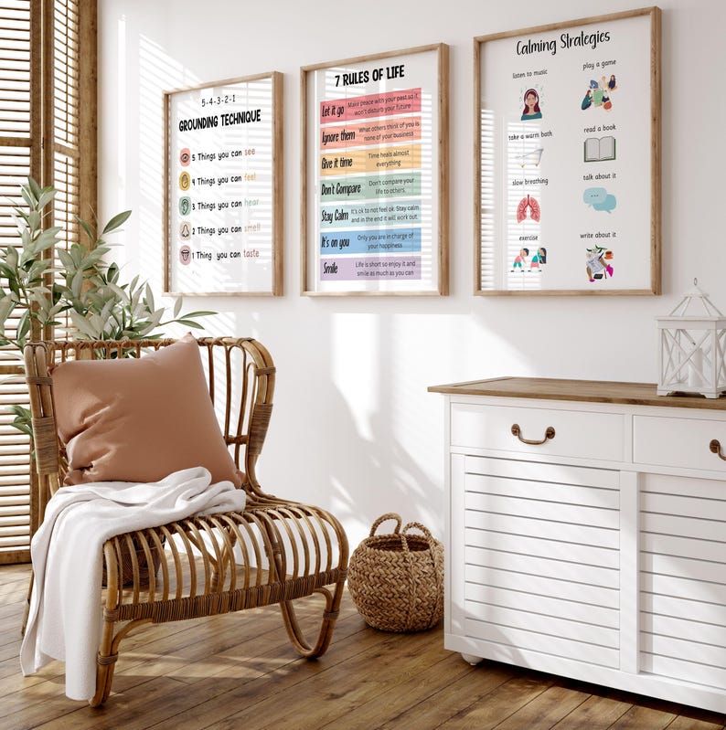 Puede incluir: Tres impresiones enmarcadas con texto: "5-4-3-2-1 Grounding Technique", "7 Reglas de la Vida" y "Estrategias Calmantes". Cuelgan sobre un mueble blanco y una silla de mimbre con un coj&iacute;n y una manta. Una cesta tejida est&aacute; en el suelo de madera.