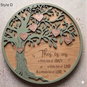 May include: A wooden family tree wall decor with a light green tree design and pink heart-shaped name tags. The text "This is us" and other phrases are engraved on the wooden background. The tree is set in a round frame.