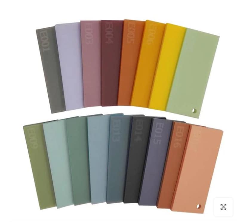 May include: A collection of rectangular color swatches in various shades, including gray, purple, red, orange, yellow, and green. Each swatch is labeled with a code and has a small hole. The swatches are arranged in two rows.