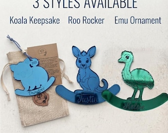 May include: Three acrylic animal ornaments labeled 3 STYLES AVAILABLE: Koala Keepsake, Roo Rocker, and Emu Ornament. The blue koala features the name Theodore and year 2025, the blue kangaroo features the name Justin, and the green emu features the name Kelsie.