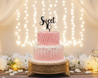 May include: A two-tier pink cake with white drip icing, topped with a black script cake topper that reads Sweet 16. The cake is decorated with small gold sprinkles and white flowers, resting on a round gold pedestal stand with ornate feet.