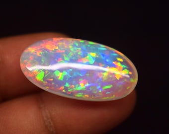 May include: An oval-shaped opal gemstone with a vibrant display of colors. The opal showcases a play-of-color effect, with flashes of red, orange, yellow, green, and blue. The gemstone is set against a dark background.