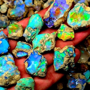 Könnte beinhalten: Eine Sammlung roher Opal-Edelsteine mit leuchtenden Farben wie Blau, Grün und Orange. Die Opale sind vor einem Hintergrund aus brauner Matrix platziert, was ihre natürliche, rohe Schönheit hervorhebt. Diese Edelsteine eignen sich ideal für die Schmuckherstellung.