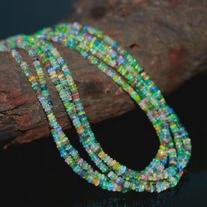 May include: A collection of colorful opal bead necklaces. The beads display a range of colors, including green, blue, yellow, and pink. The necklaces are draped over a piece of dark brown wood, creating a striking contrast.