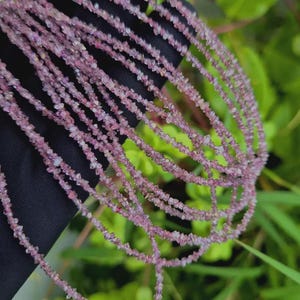 Peut inclure: Un long collier composé de petites pépites de pierres précieuses brutes de couleur rose violacé. Les perles présentent une texture irrégulière et dentelée avec un aspect translucide, formant une chaîne continue de fragments naturels mauves.