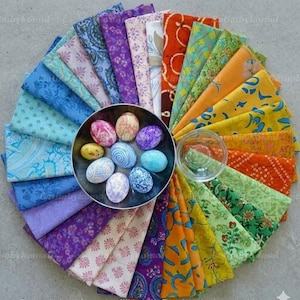 Peut inclure: Une composition circulaire de coupons de tissu colorés entoure un bol en métal contenant des œufs de Pâques décorés. Les tissus présentent divers motifs et teintes, notamment des bleus, des violets, des oranges et des verts. Un petit bol en verre est également présent.