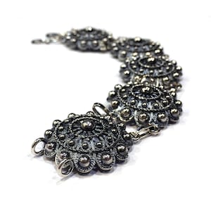 May include: A silver bracelet with a series of ornate, circular, filigree designs. The bracelet is made of metal and has a dark, oxidized finish.