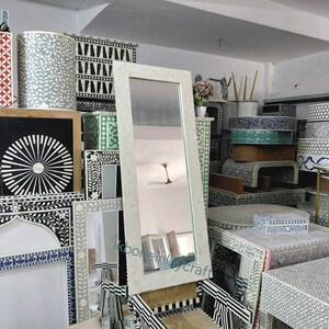 May include: A selection of decorative furniture, including mirrors, tables, and boxes, is shown. The items have detailed inlaid patterns in black, white, and other colours. A large, rectangular mirror with a light-coloured frame is a prominent feature.