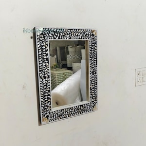 Puede incluir: Un espejo de pared rectangular con un marco decorativo. El marco presenta un patrón floral en blanco y negro. El espejo está montado en una pared blanca. La marca "ikbonei" es visible en la esquina superior izquierda.