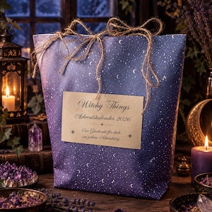 Könnte beinhalten: Eine violette Geschenktüte mit einem weißen Himmelsmuster aus Sternen und Mondsicheln, die mit einer braunen Kordelschleife gebunden ist. Ein rechteckiges beiges Etikett auf der Vorderseite trägt den Text Witchy Things Adventskalender 2026 und Ein Geschenk für dich, an jedem Adventstag.