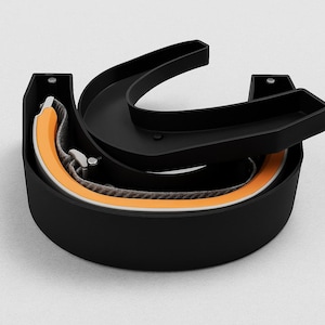 May include: A black, semi-circular case with a hinged lid, holding a folded, orange-trimmed item. The item has a gray, woven strap and a silver clasp. The case is on a white surface.