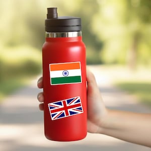 May include: A bright red reusable water bottle with a black lid and a straw spout. The bottle features two rectangular stickers: one displaying the saffron, white, and green flag of India with a blue wheel, and another showing the Union Jack flag of the UK.