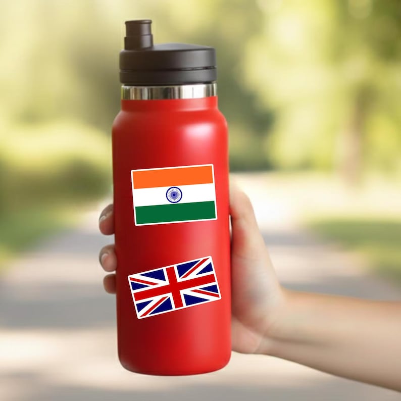 May include: A bright red reusable water bottle with a black lid and a straw spout. The bottle features two rectangular stickers: one displaying the saffron, white, and green flag of India with a blue wheel, and another showing the Union Jack flag of the UK.